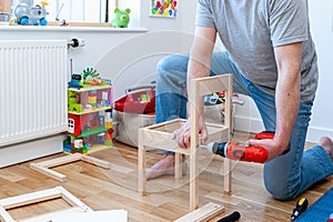 A male adult person assembling from flat-pack a set of two small chairs with desk.