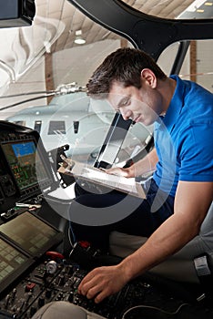 Male Aero Engineer With Clipboard Working In Helicopter Cockpit