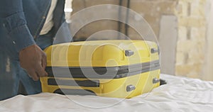 Male African American hands zipping yellow travel bag lying on white bedding. Unrecognizable male tourist packing
