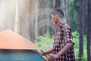 Male African-Asian tourist setting up the tent at the forest.