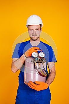 A male air conditioning repairman is holding a freon cylinder in his hands to air-condition the air conditioner