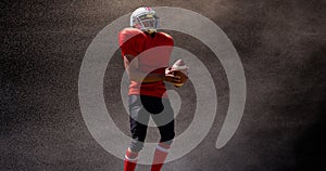 Male american football player holding ball against black background with mist