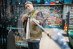Male angler choosing rod in fishing shop