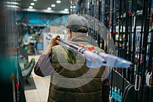 Male angler holds rod with reel in fishing shop