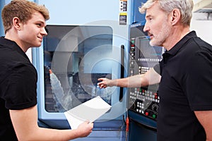 Male Apprentice Working With Engineer On CNC Machinery