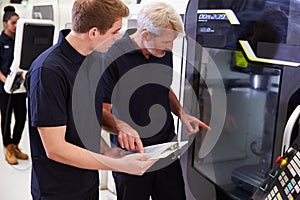 Male Apprentice Working With Engineer On CNC Machinery