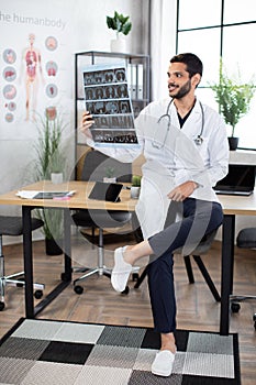 Male Arab doctor, leaning on the table in modern office, looking at computer tomograph scan.