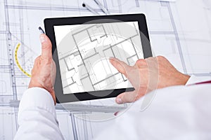 Male architect analyzing blueprint over digital tablet