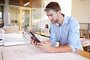 Male Architect With Digital Tablet Studying Plans In Office