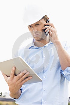Male architect with digital tablet using cell phone at site