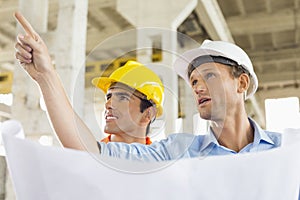 Male architect explaining building plan to colleague at construction site