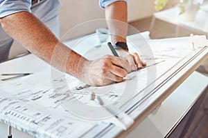 Male architect hands drawing building project or construction plan on an office table. Closeup of caucasian man taking