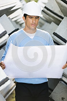 Male architect reviewing blueprint at construction site