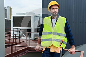 male architect in safety vest and hardhat with tool belt standing