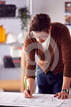 Male Architect Standing At Desk In Office Amending Building Plans