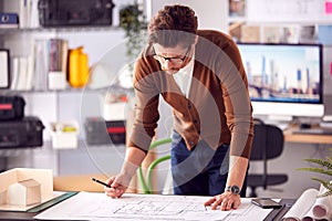 Male Architect Standing At Desk In Office Amending Building Plans