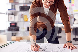 Male Architect Standing At Desk In Office Amending Building Plans