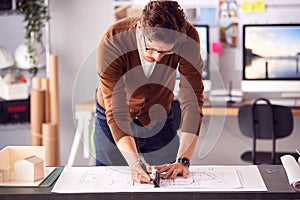 Male Architect Standing At Desk In Office Amending Plan Or Blueprint With Ruler