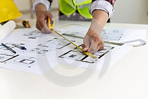 The male architect uses a tape measure to measure the house designs.