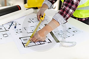 The male architect uses a tape measure to measure the house designs