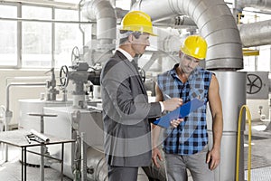 Male architect with worker discussing over clipboard in industry