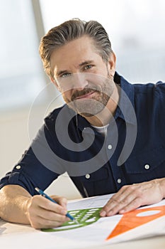 Male Architect Working On Blueprint At Desk