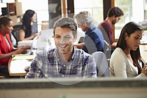 Male Architect Working At Desk With Meeting In Background