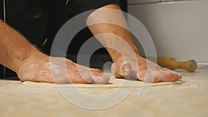 Male arms of cook forming pastry on a wooden surface at restaurant. Hands of chef shaping floured dough for pizza on a