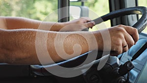 Male arms of lorry driver holds a big steering wheel while driving a truck at sunny day. Trucker riding to destination