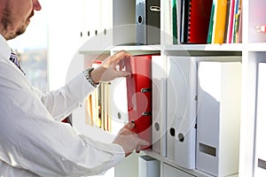 Male arms pick red file folder from office book shelf