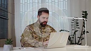 Male army soldier using computer for emailing and working while sitting at home