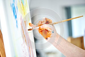 Male artist hand, holding brush and painting rich orange paint.