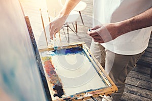 Male artist mixes colors on the palette in studio. Painter in workshop photo