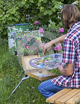 Male artist paint on plein air flowers pink peonies painting on nature