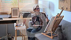 Male artist painting picture on easel in living room.