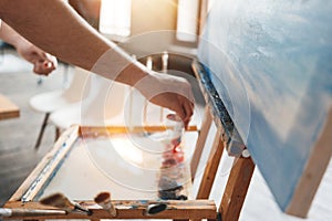 Male artist work in art studio. Hand of painter closeup squeezing paint from a tube on a palette