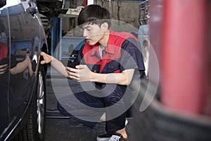 Male Asian automotive mechanical worker checks tire pressure at a car garage.
