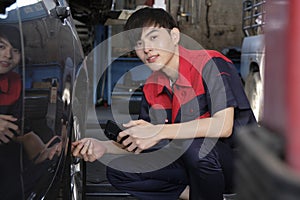 Male Asian automotive mechanical worker checks tire pressure at a car garage.