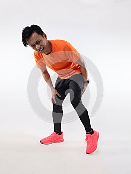 Male Asian runner having rear leg pain, hamstring muscle cramp because of not doing warm up before run exercise. High key studio