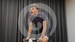 Male athlete cycling out of saddle on smart bike trainer. Close up of young boy pedaling on bicycle at home. Indoors virtual cycli
