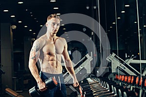 Male athlete with a dumbbell in the gym lean on