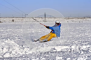 A male athlete engaged in snow kiting on the ice of a large snowy lake. He goes skiing in the snow.