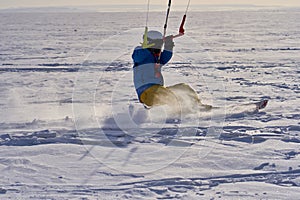 A male athlete engaged in snow kiting on the ice of a large snowy lake. He goes skiing in the snow.