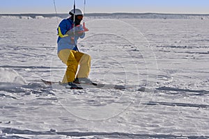 A male athlete engaged in snow kiting on the ice of a large snowy lake. He goes skiing in the snow.