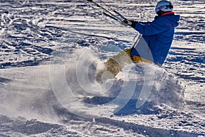A male athlete engaged in snow kiting on the ice of a large snowy lake. He goes skiing in the snow.