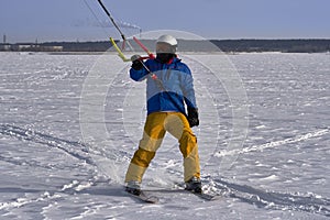 A male athlete engaged in snow kiting on the ice of a large snowy lake. He goes skiing in the snow. Winter sunny frosty day