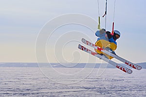 A male athlete engaged in snow kiting on the ice of a large snowy lake. He performs the jump. Winter sunny frosty day