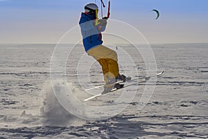 A male athlete engaged in snow kiting on the ice of a large snowy lake. He performs the jump. Winter sunny frosty day