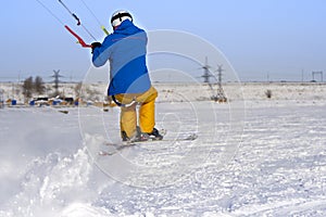 A male athlete engaged in snow kiting on the ice of a large snowy lake. He performs the jump. Winter sunny frosty day.