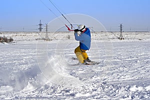 A male athlete engaged in snow kiting on the ice of a large snowy lake. He performs the jump. Winter sunny frosty day.